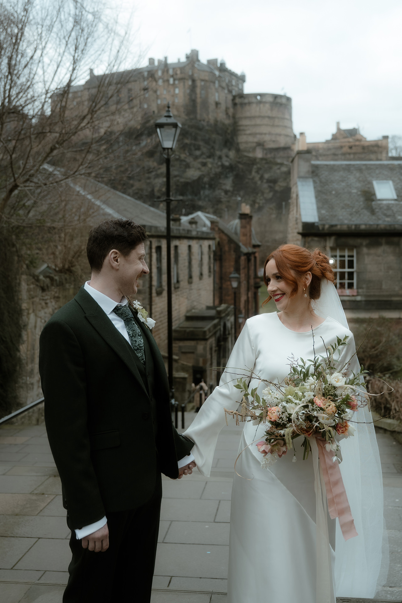 Bride and groom smiling at each other at the Vennel Steps with Edinburgh Castle in the background