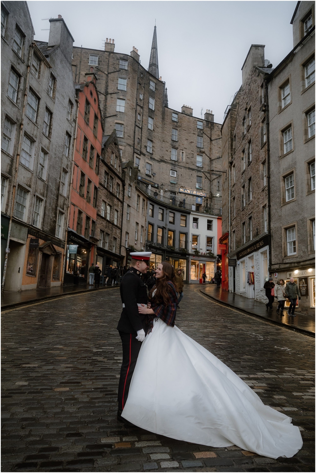 Bride and groom on a quiet cobbled street at Victoria Street, Edinburgh, with dramatic Old Town buildings rising behind them on a grey winter afternoon.