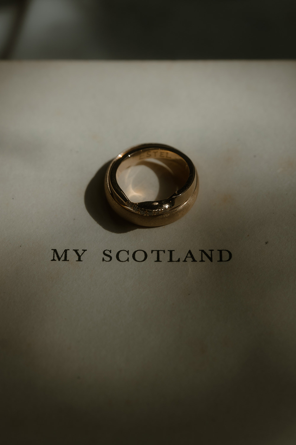 Close-up of vintage gold wedding band on book page titled ‘My Scotland’ in dramatic natural light