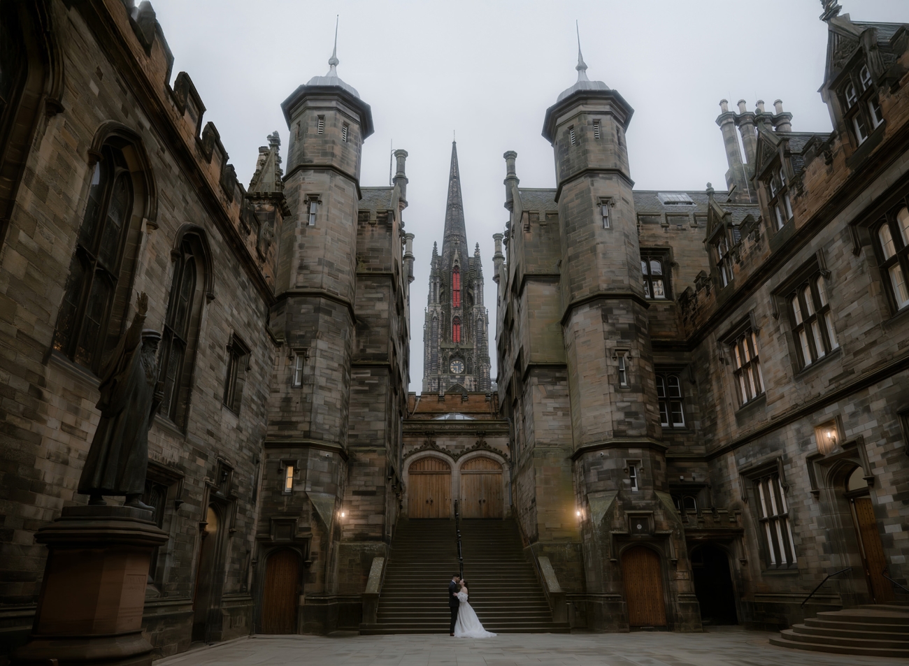 Wide perspective wedding portrait of a newlywed couple with towers of Edinburgh New College above them