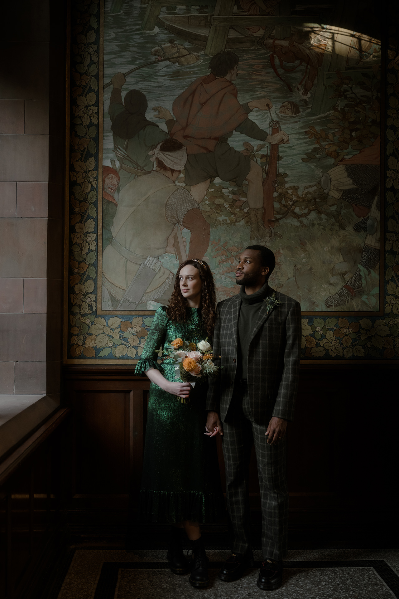 Bride and groom looking out the window at Edinburgh National Portrait Gallery - groom wearing a tweed checked suit and the bride wearing a glittery emerald dress