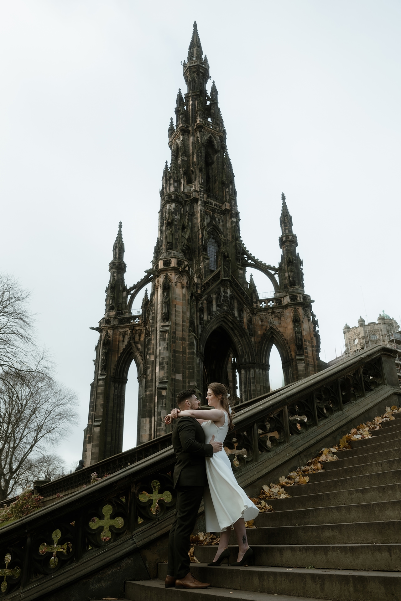 Bride and groom sharing an embrace on a windy day with the Scott's Monument behind them