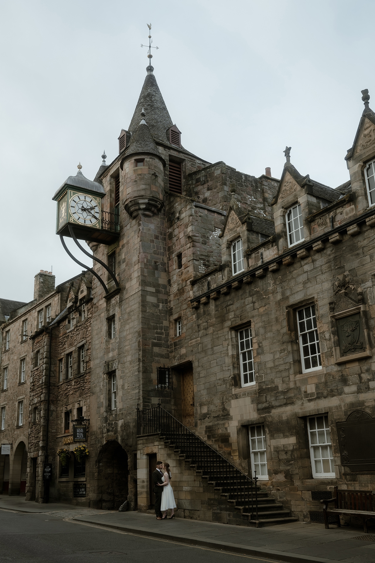Newlyweds sharing a kiss in front of one of Royal Mile's oldest buldings, with the big clock towering above them