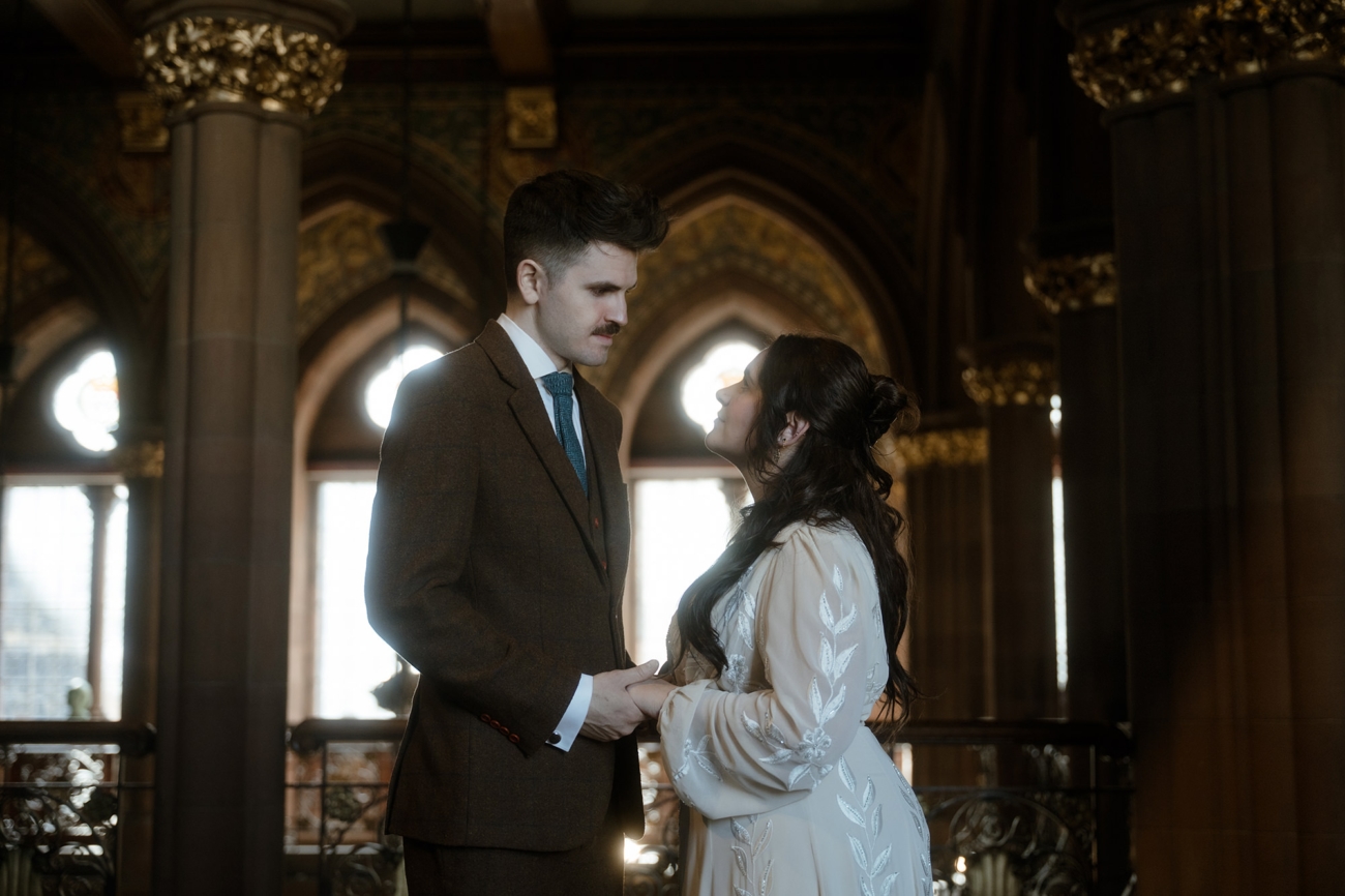 Eloping couple standing in the Scottish National Portrait Gallery of Edinburgh, holding hands and looking at each other