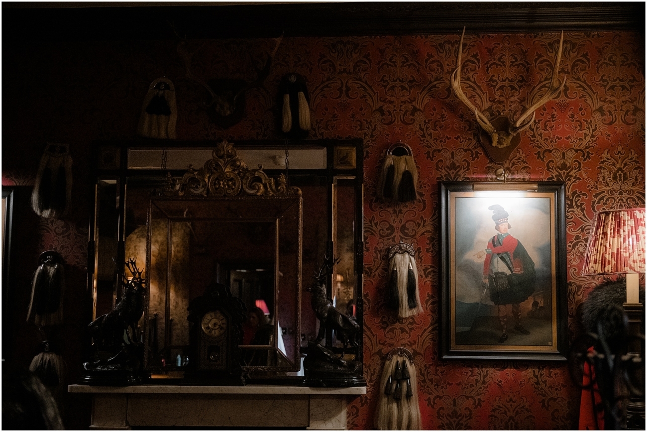 Gothic interior of The Witchery’s suite with red damask wallpaper, antlers, and vintage military portrait - the Witchery weddings in Edinburgh.