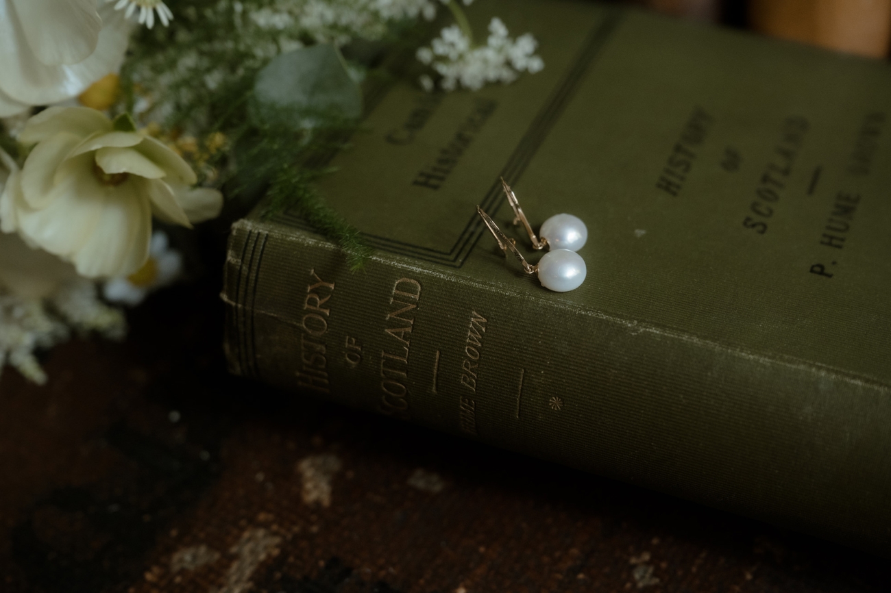Vintage pearl drop earrings on antique ‘History of Scotland’ book with ivory florals—romantic Scottish wedding flat-lay