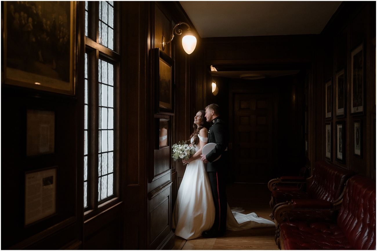 Bride and groom standing in a wood-panelled hallway, softly lit from a stained glass window, sharing an intimate moment during their Edinburgh winter wedding.