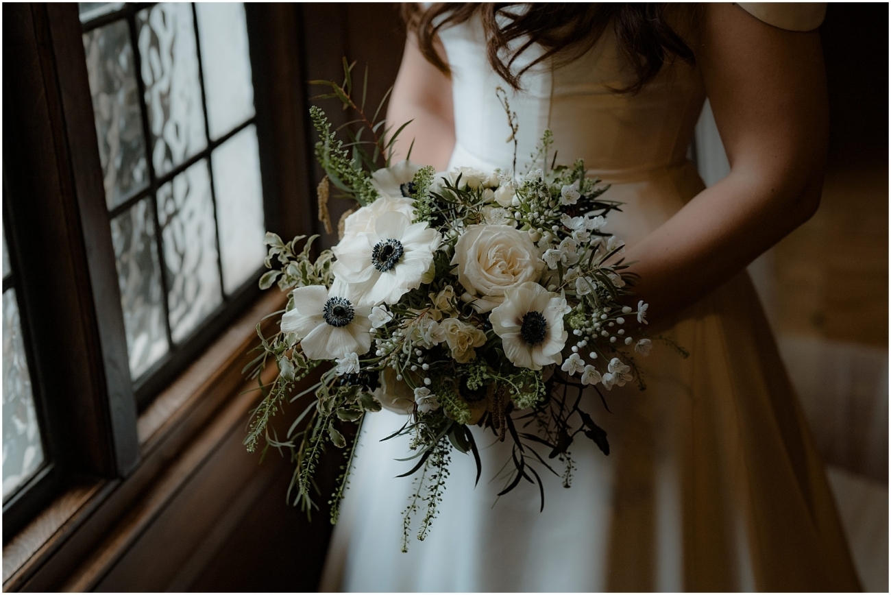 Close-up of the bridal bouquet featuring white roses, anemones, and seasonal greenery, placed against a leaded glass window in a historic Edinburgh venue.