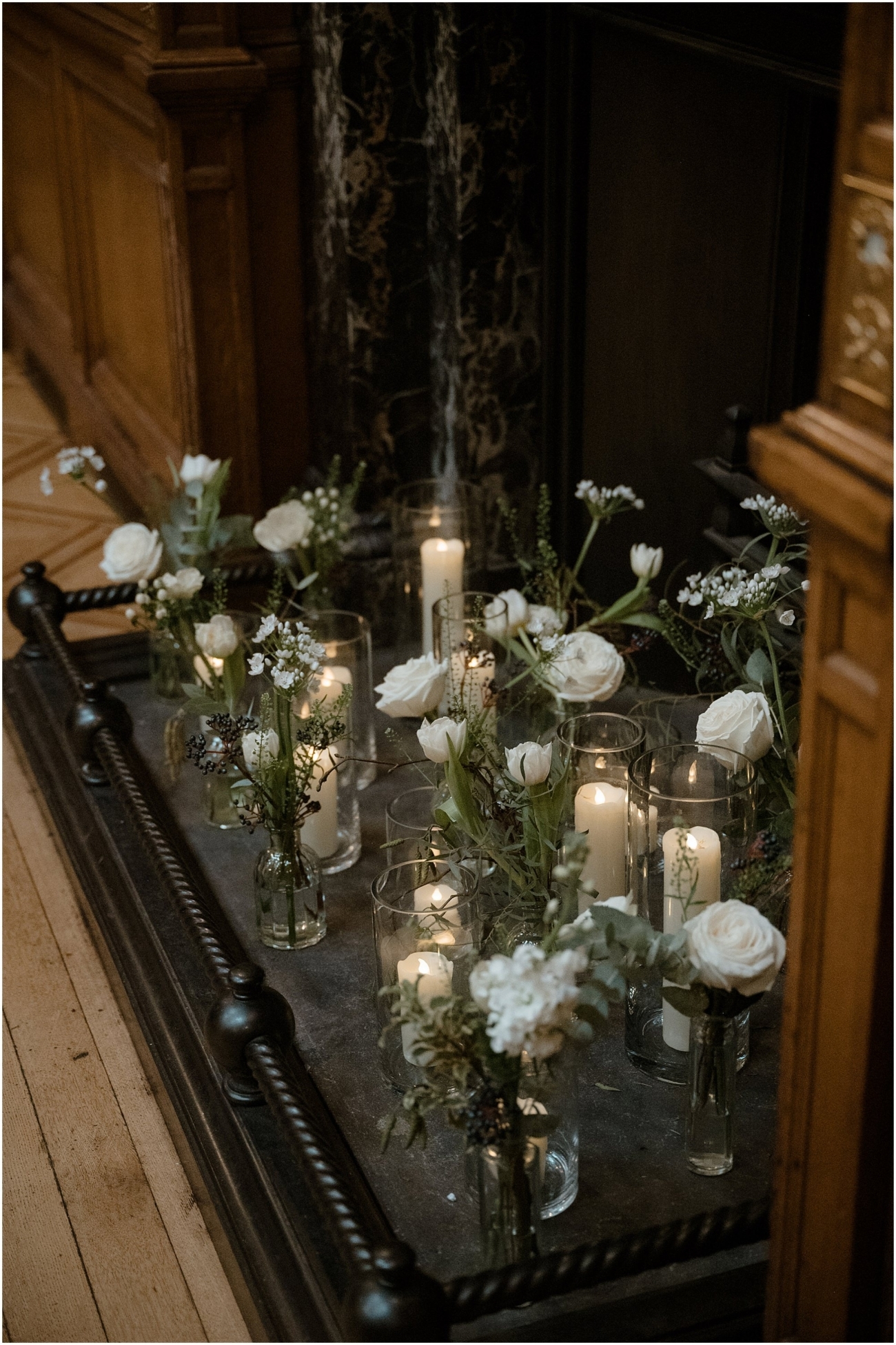 Detail shot of white roses, baby’s breath, and candlelight arranged in glass vases at the fireplace altar during an Edinburgh winter wedding ceremony.