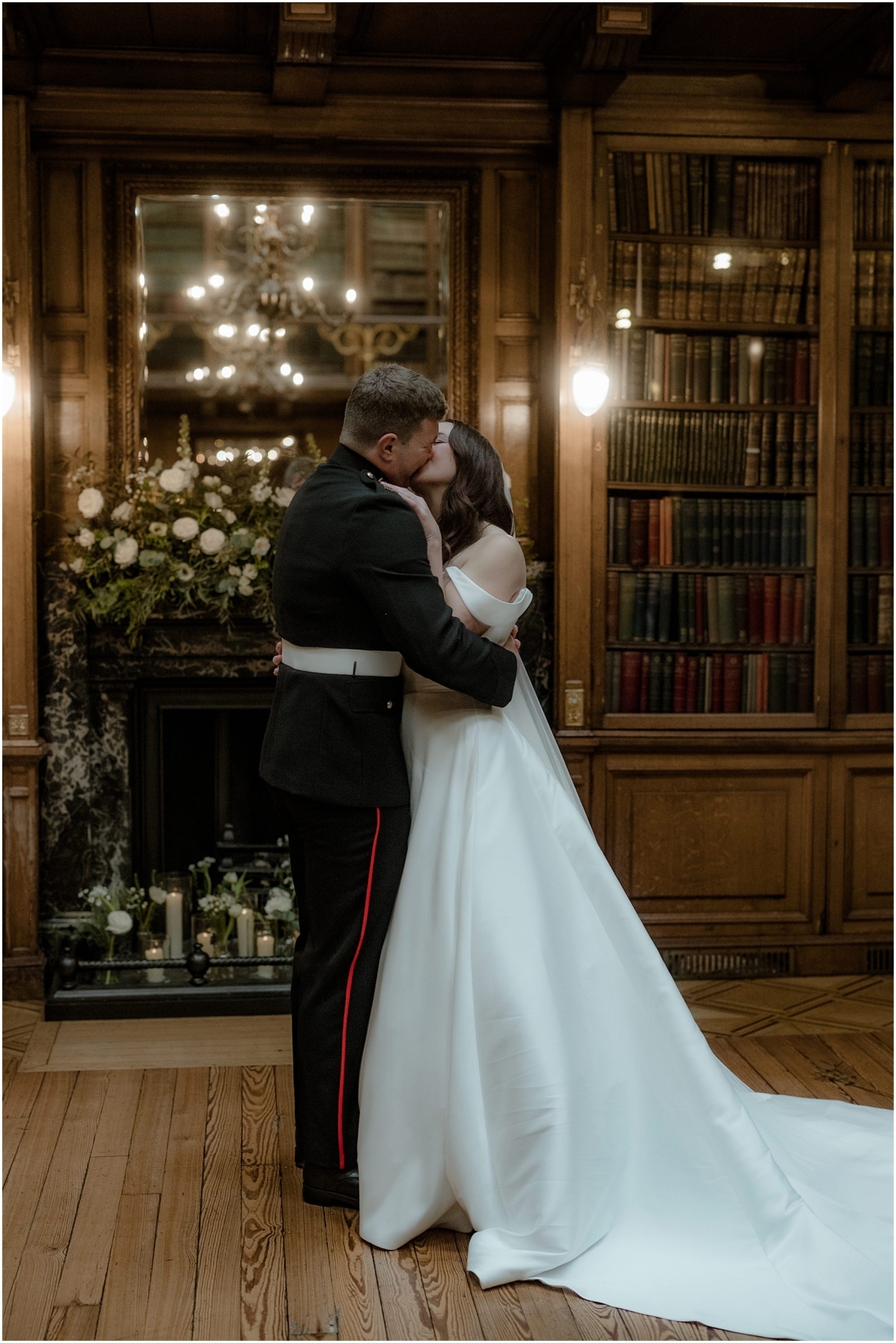 Bride and groom share their first kiss in front of a mirror and fireplace adorned with fresh flowers and candles