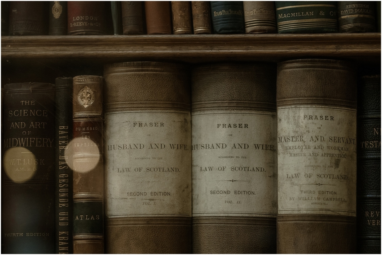 A close-up of old leather-bound books in the library shelves, prominently featuring titles like Fraser on Husband and Wife.