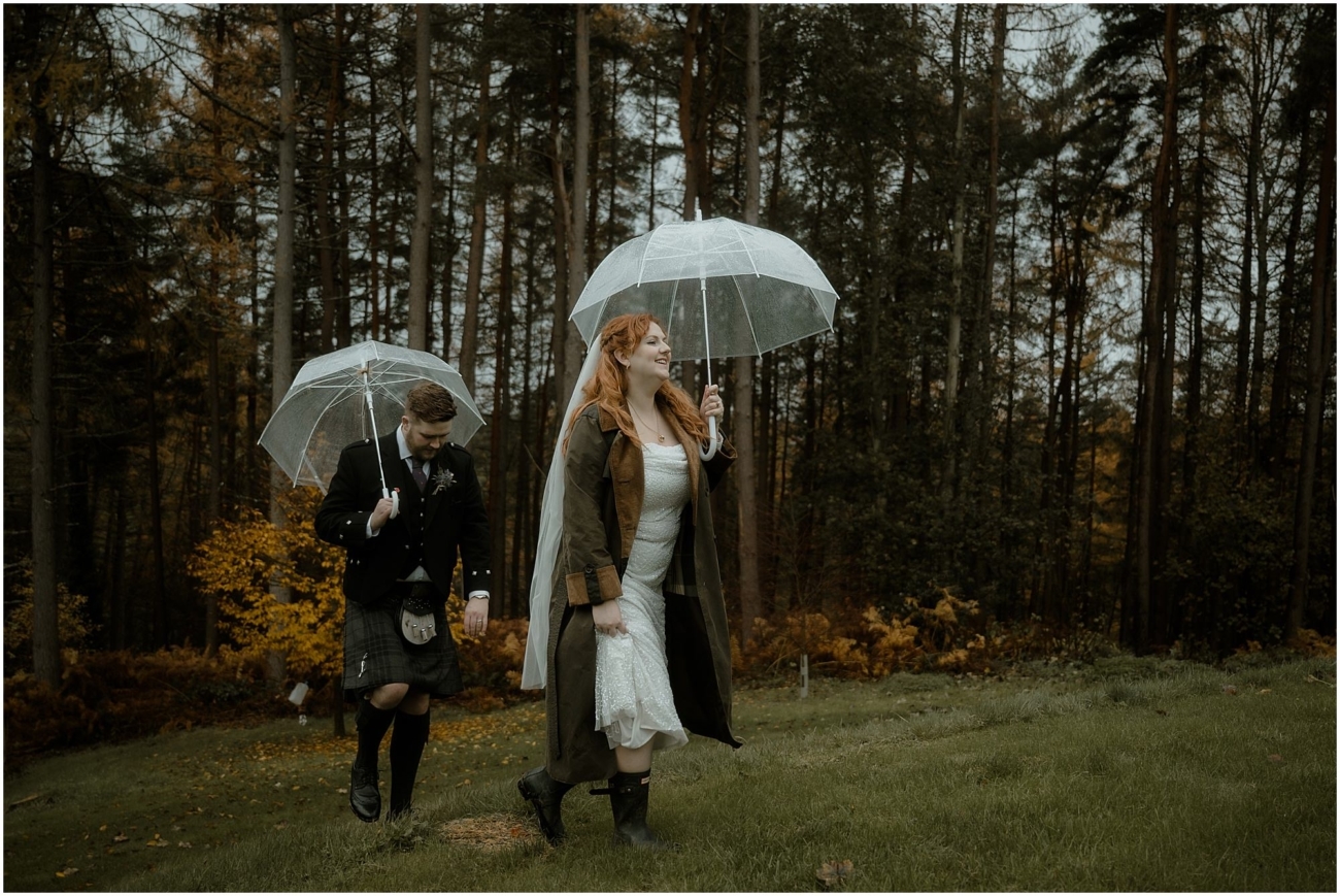 Cosy & Intimate Wedding at Ferniehirst Castle in the Scottish Borders 27 Bride and groom walking away from the forest, uphill with umbrellas