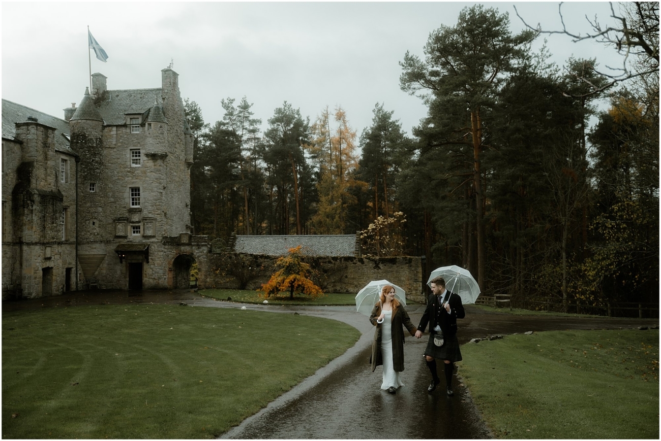 Cosy & Intimate Wedding at Ferniehirst Castle in the Scottish Borders 20 Bride and groom walking together in the rain at Ferniehirst Castle with umbrellas