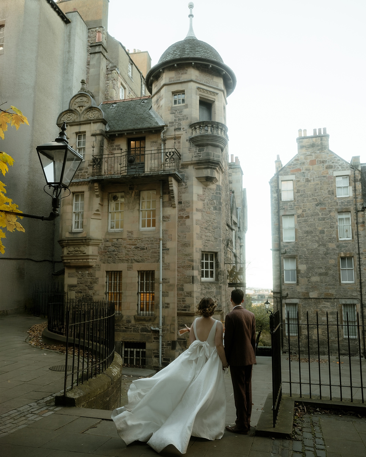 Bride and groom holding hands in front of Edinburgh Writer's Museum, bride's dress flowy in the wind