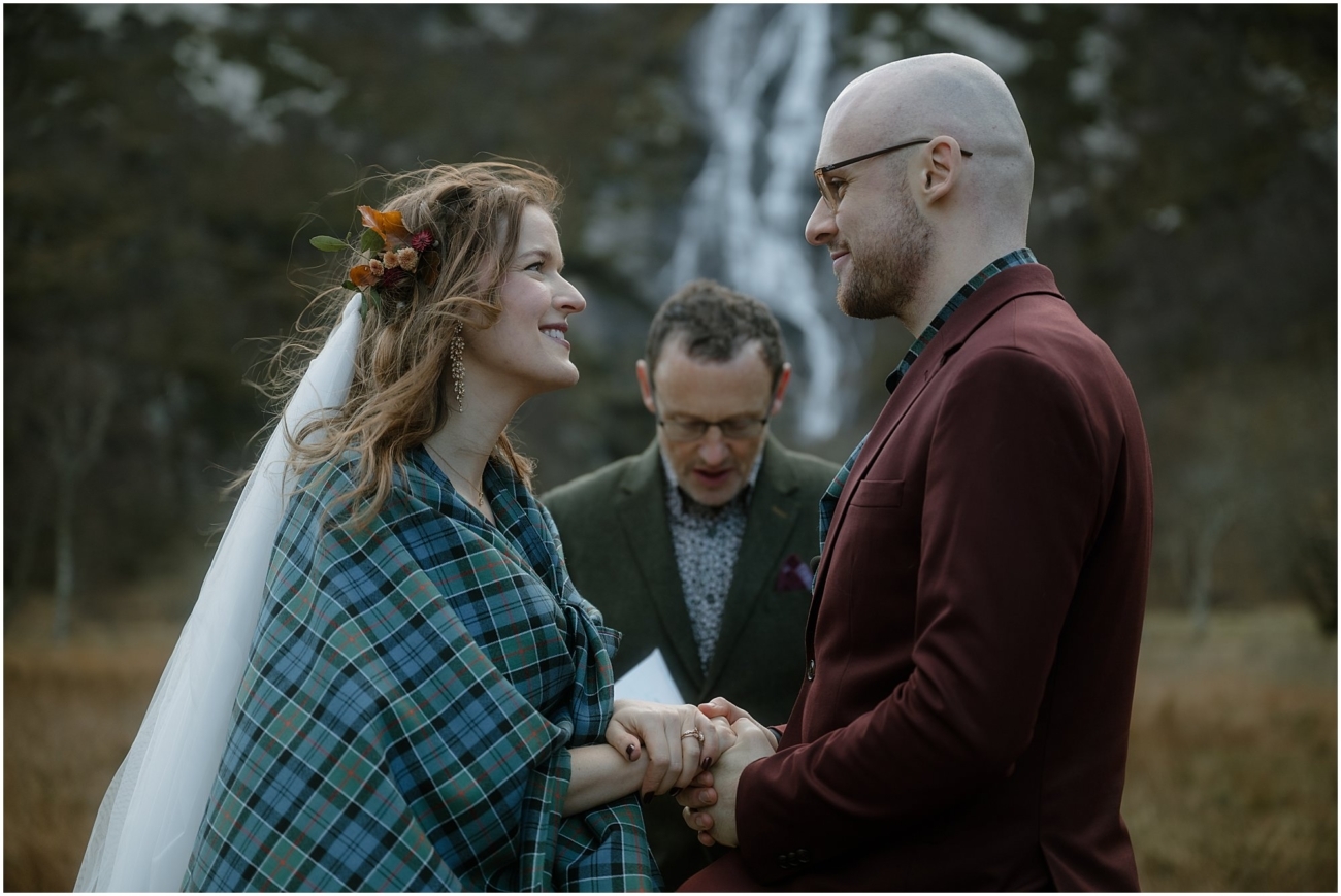 Steall Falls elopement in Glen Nevis 9 A closer moment in the ceremony: the couple gaze at each other, hands held, as the officiant speaks. The bride is wrapped in tartan and wearing a floral crown
