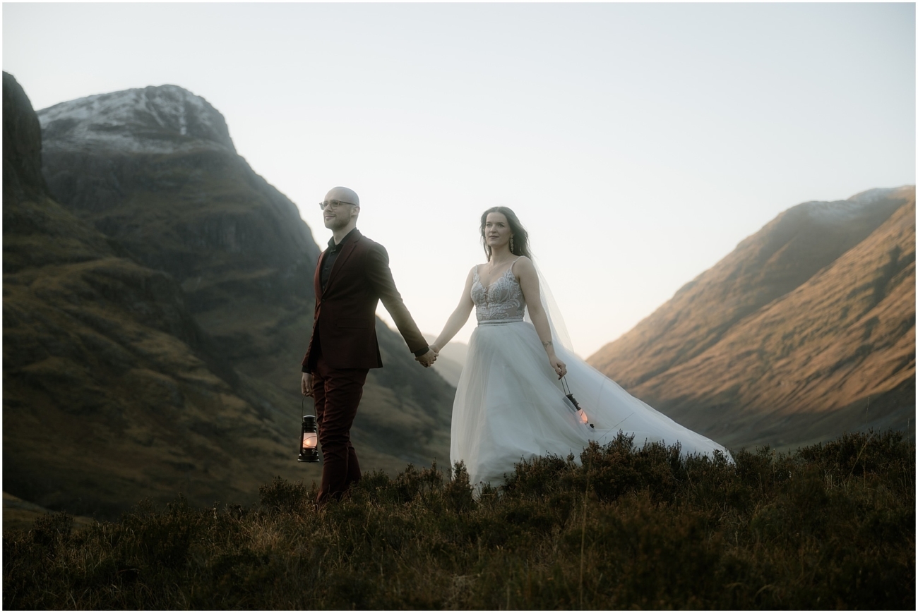 Steall Falls elopement in Glen Nevis 44 The couple stands hand in hand on a grassy hill, each holding a lit lantern. The bride’s flowing dress catches the golden light of the setting sun