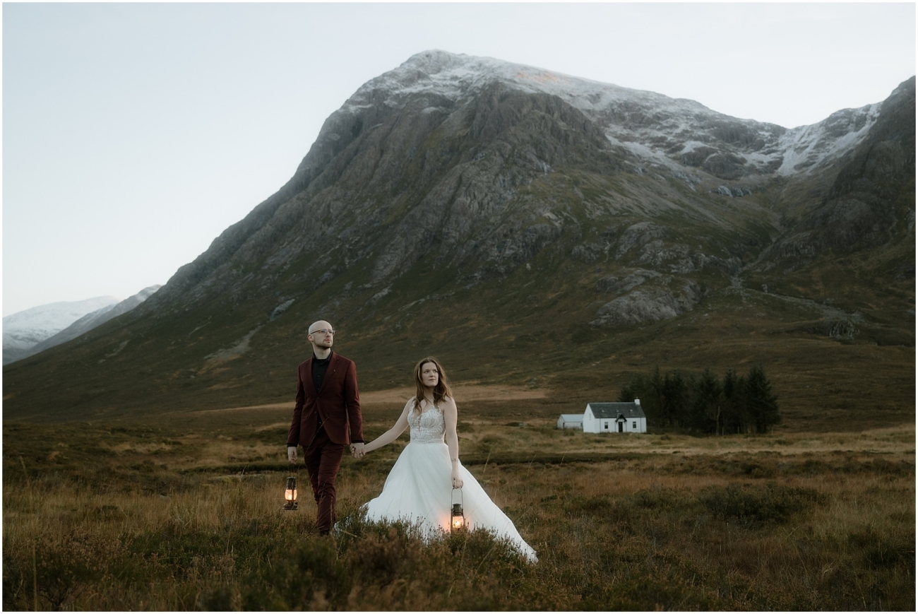 Steall Falls elopement in Glen Nevis 48 A wider landscape view shows the couple walking through the moorland, lanterns in hand, with the iconic white cottage of Glencoe in the background