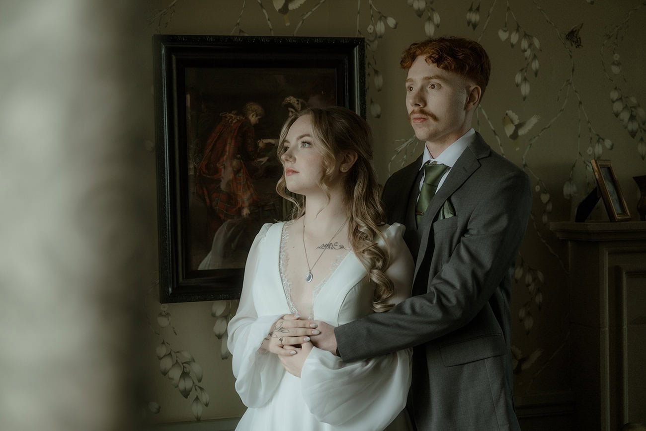 Bride and groom sharing a quiet moment in a beautifully decorated room at Monkstadt Hotel, Isle of Skye, a moody antique oil painting visible behind them