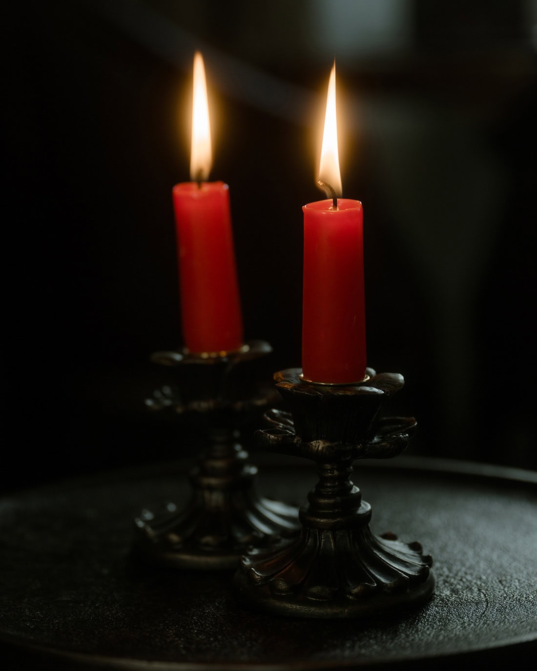 Two red candles burning on antique brass candlesticks against a dark background