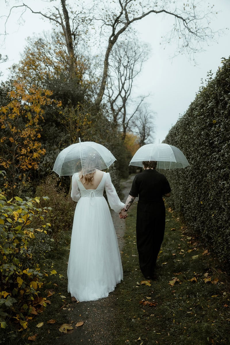 Weddings at the Royal College of Physicians Edinburgh: everything you need to know 6 Newlywed couple walking hand in hand through Queen Street Gardens Edinburgh in the rain with clear umbrellas