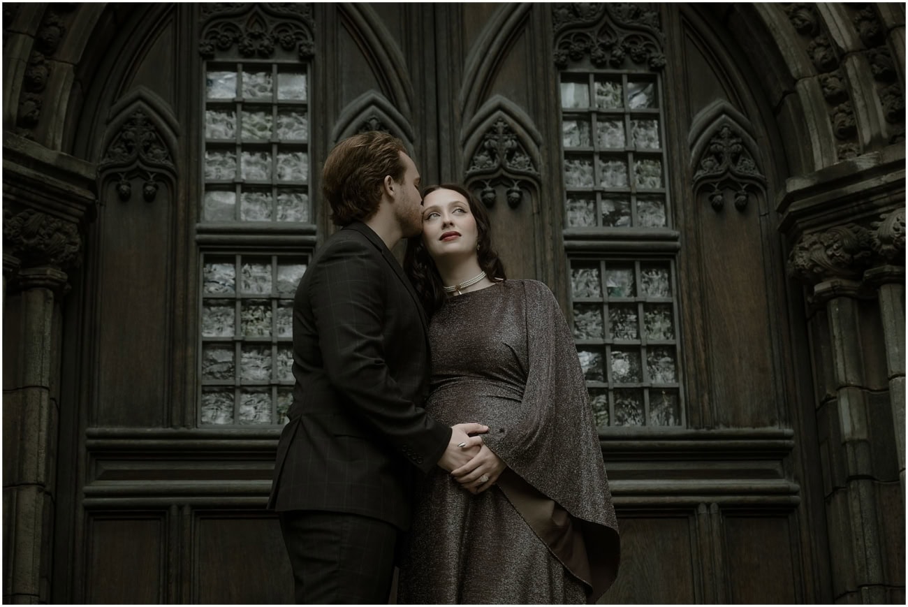 Man kissing woman's cheek outside St Giles Cathedral Edinburgh, gothic windows behind them, dark academia maternity shoot