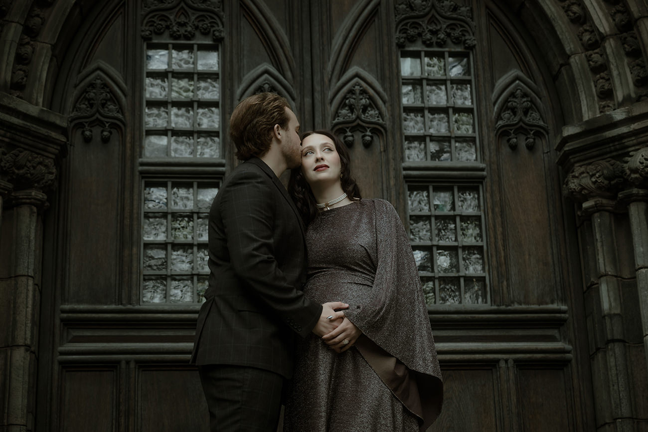 Groom kissing bride's temple in front of an ornate dark gothic stone facade of St Giles Cathedral in Edinburgh - moody gothic elopement photography Scotland