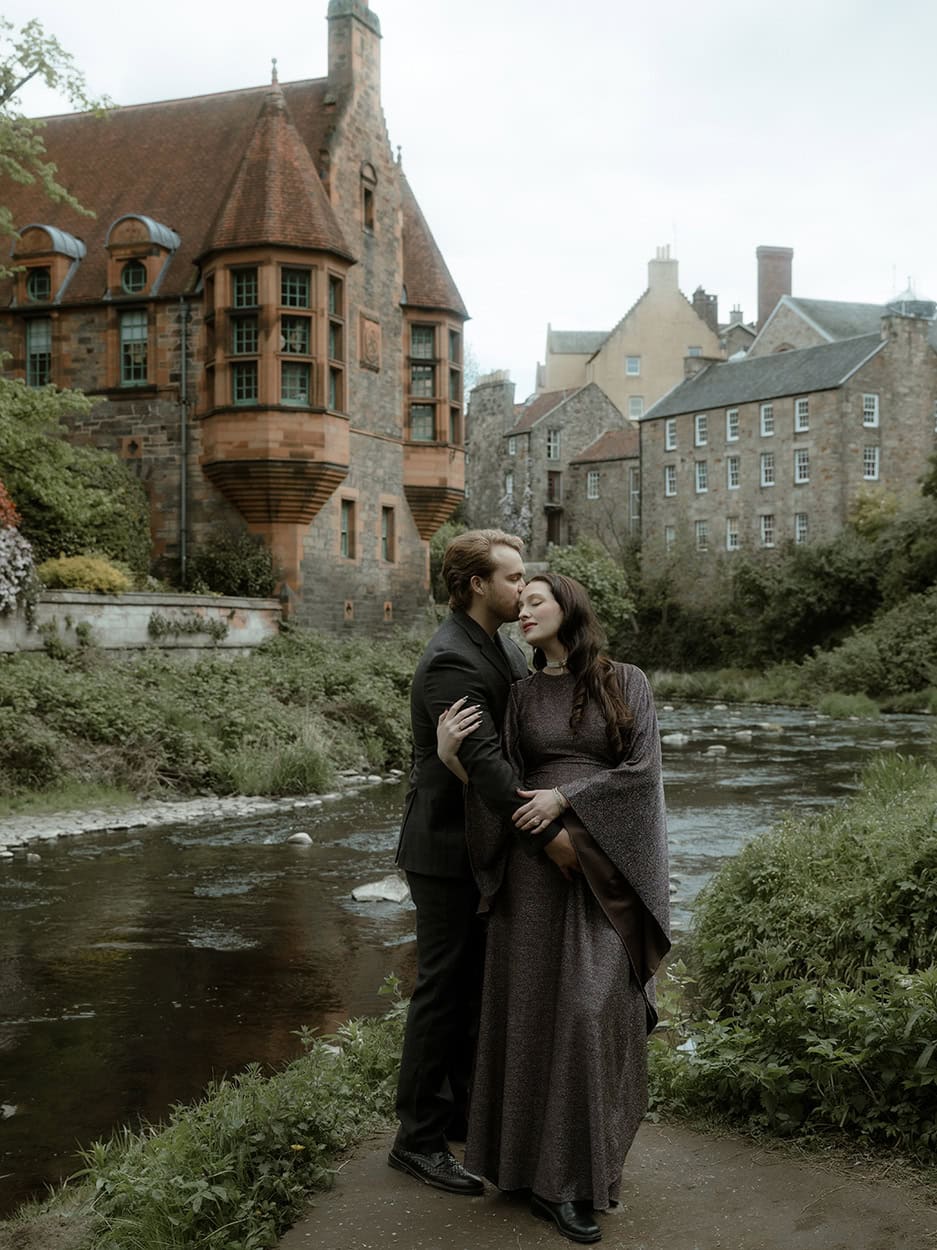 Bride leaning back into groom's arms at Dean Village Edinburgh, iron railings and the Water of Leith in the background