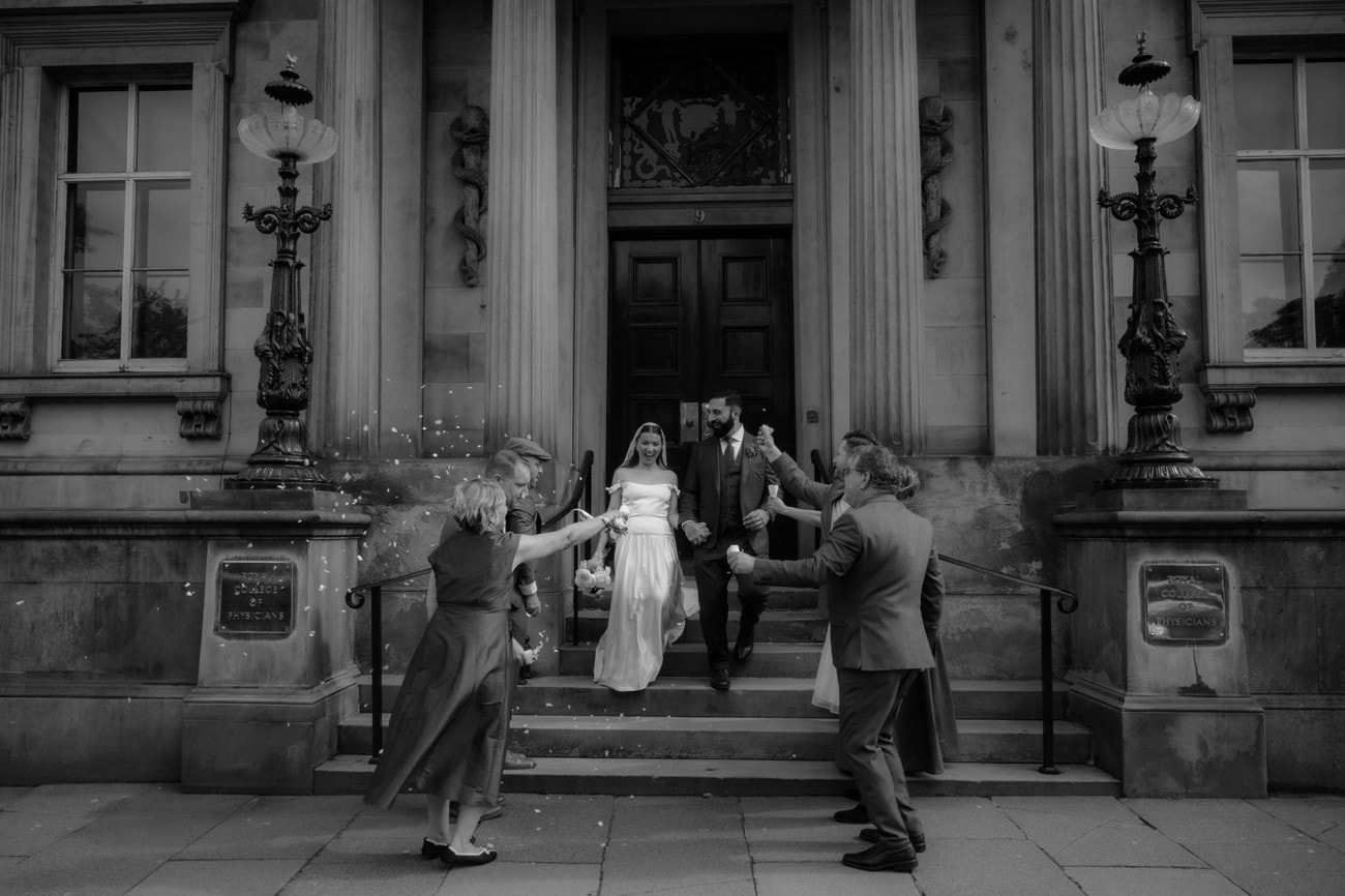 Weddings at the Royal College of Physicians Edinburgh: everything you need to know 12 Black and white photo of a bride and groom exiting the Royal College of Physicians of Edinburgh as guests throw confetti on the steps