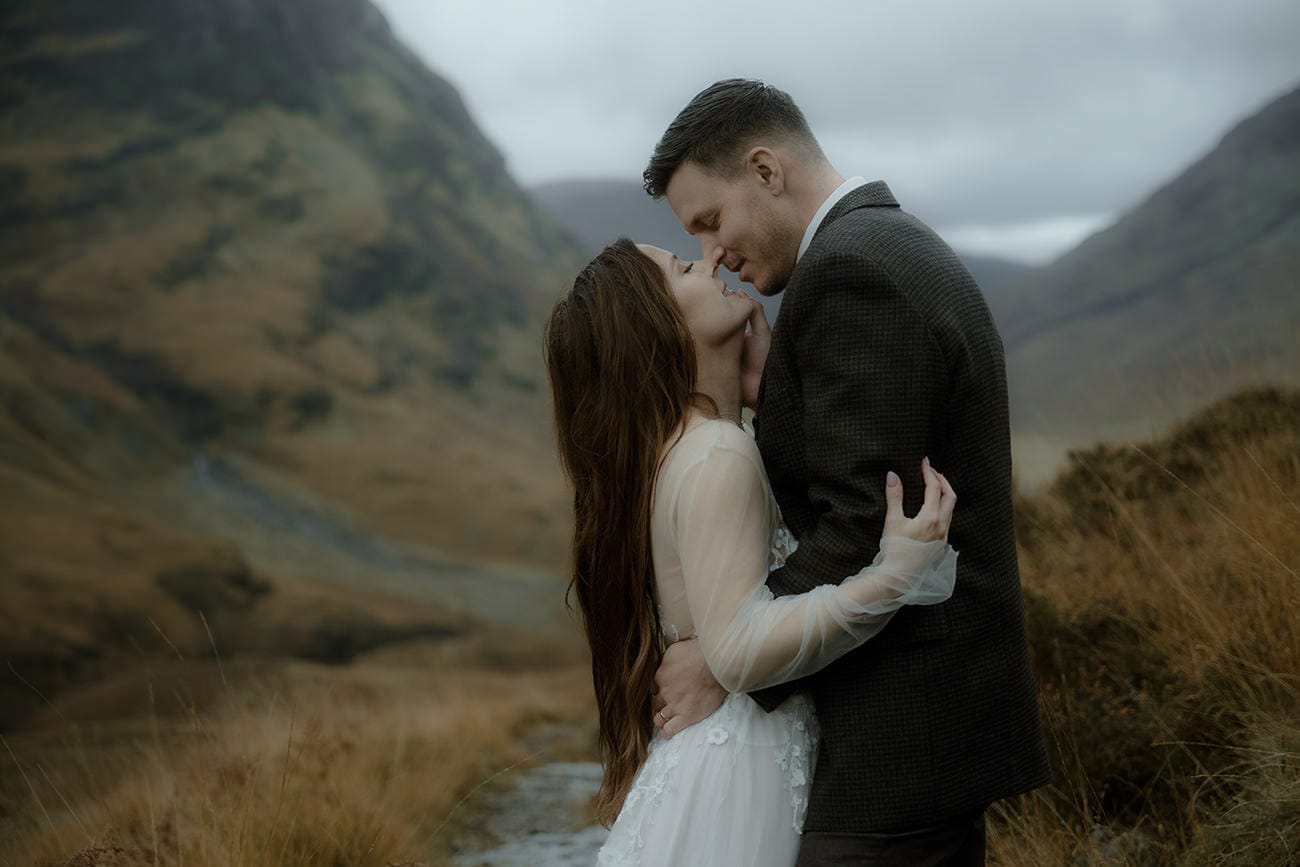 Bride and groom about to kiss in the Glencoe valley, surrounded by moody autumn moorland and cloud-covered highland mountains
