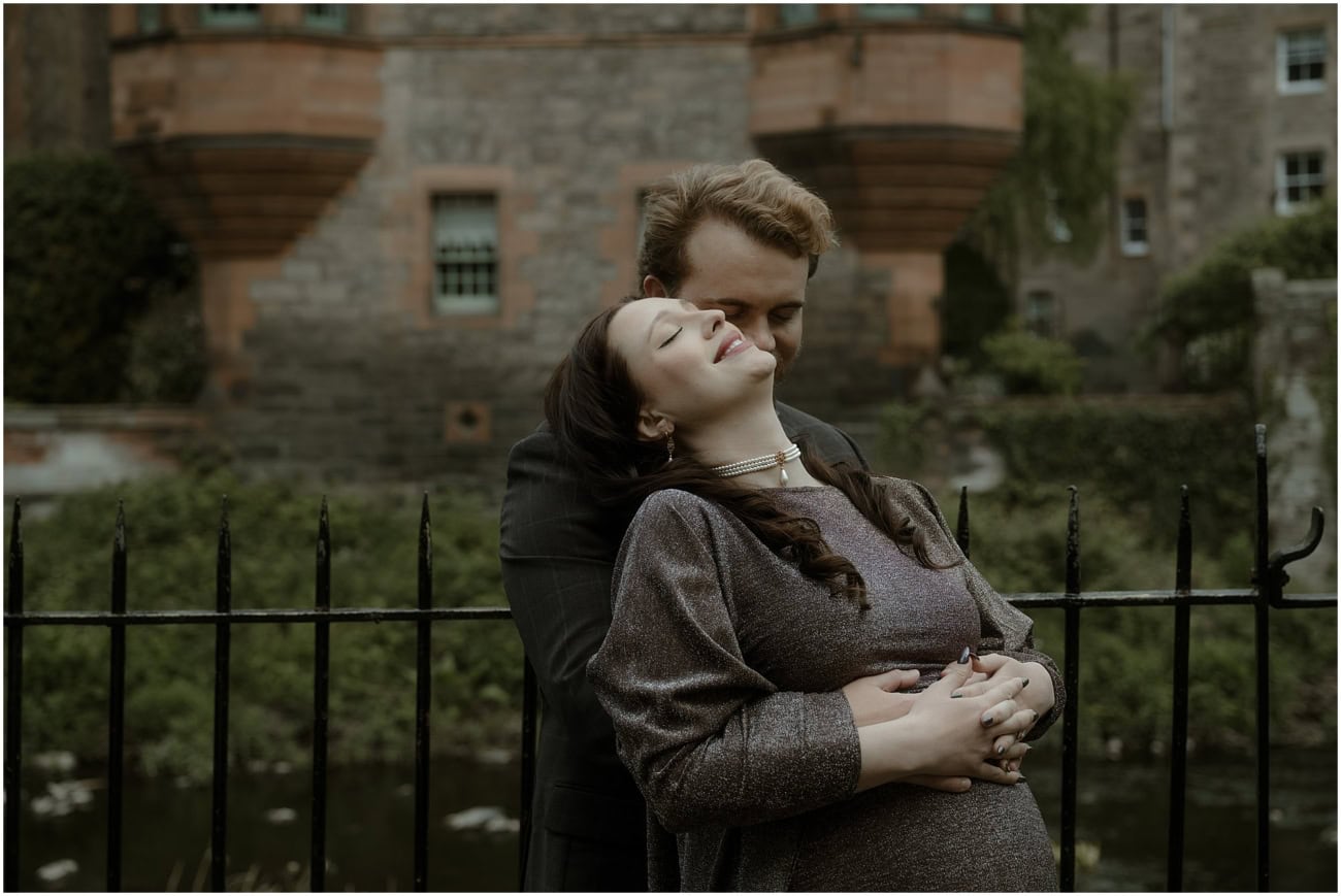 Close-up of pregnant woman laughing with head back as partner kisses her neck, Well Court tower behind in Dean Village Edinburgh