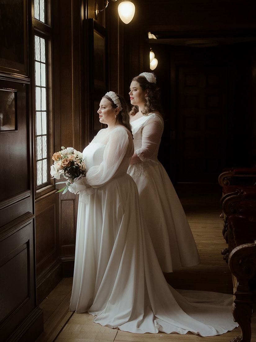 Weddings at the Royal College of Physicians Edinburgh: everything you need to know 19 Two brides standing by leaded windows in the corridor at the Royal College of Physicians Edinburgh - same-sex Edinburgh elopement