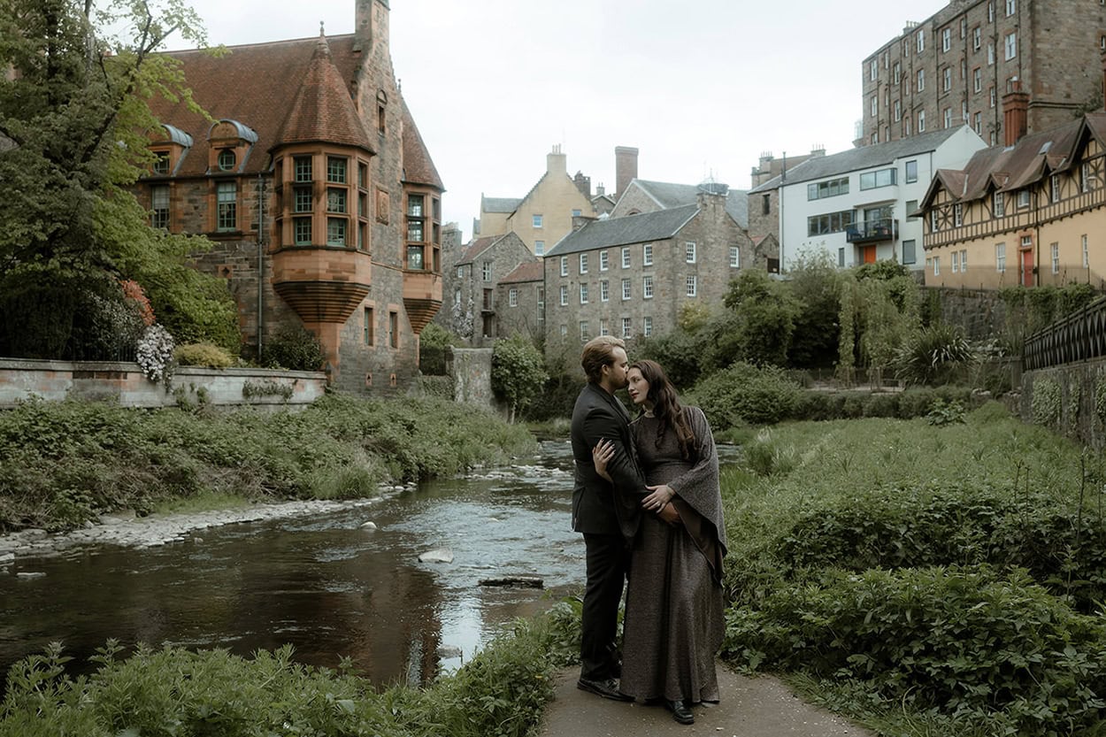 Bride leaning back into groom's arms at Dean Village Edinburgh, iron railings and the Water of Leith in the background - spring elopement in Edinburgh in May