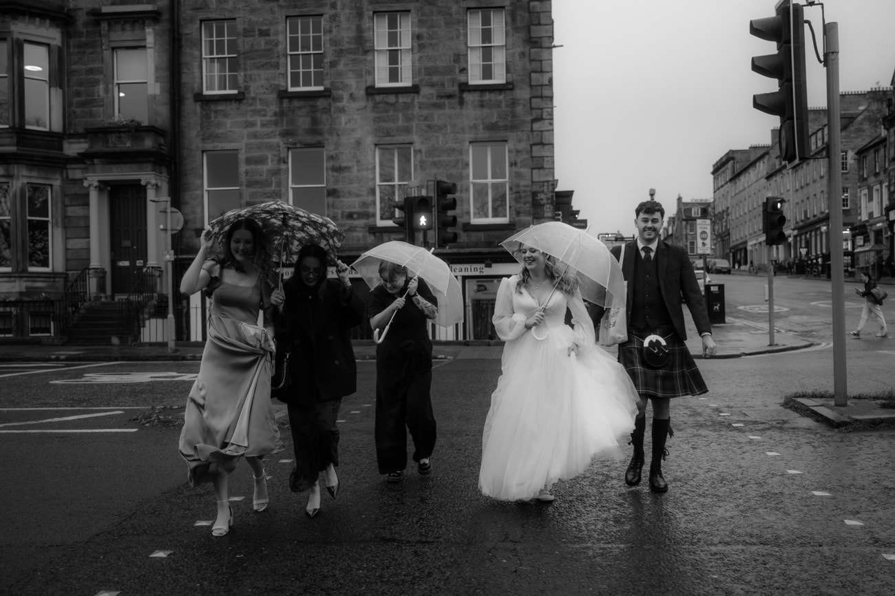 Weddings at the Royal College of Physicians Edinburgh: everything you need to know 5 Wedding party crossing the street in Edinburgh's New Town in the rain, bride in white dress and other bride in black jumpsuit